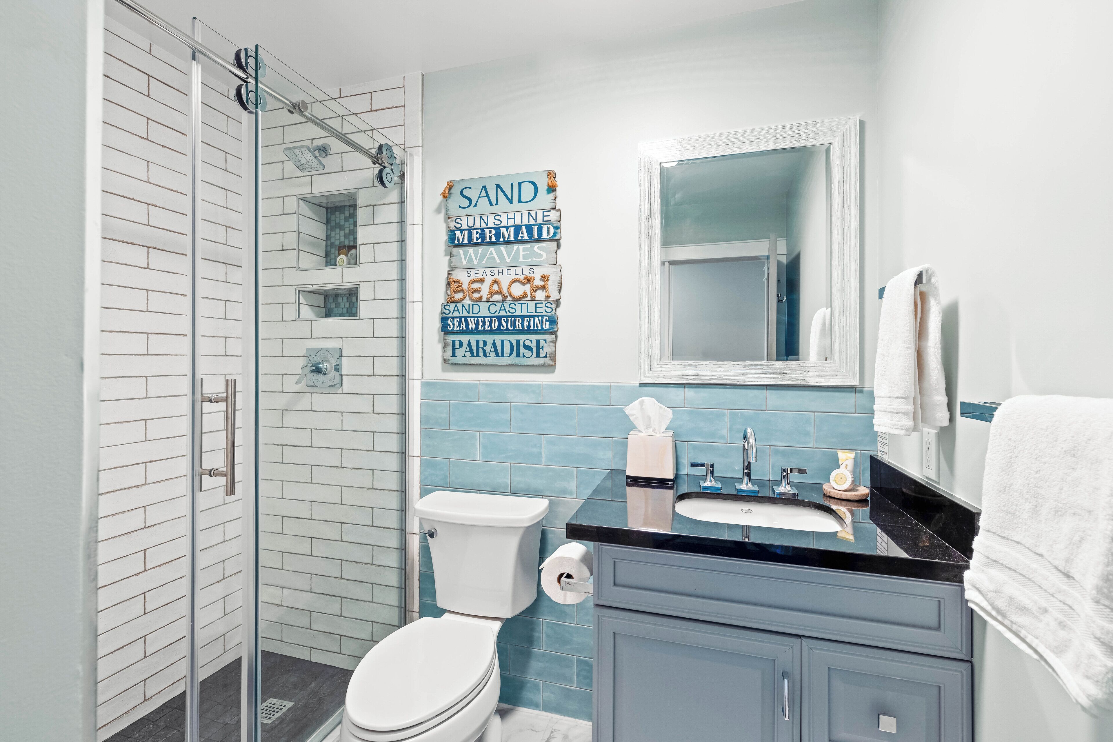 A bathroom with a glass shower enclosure, a toilet, a sink, and a mirror.