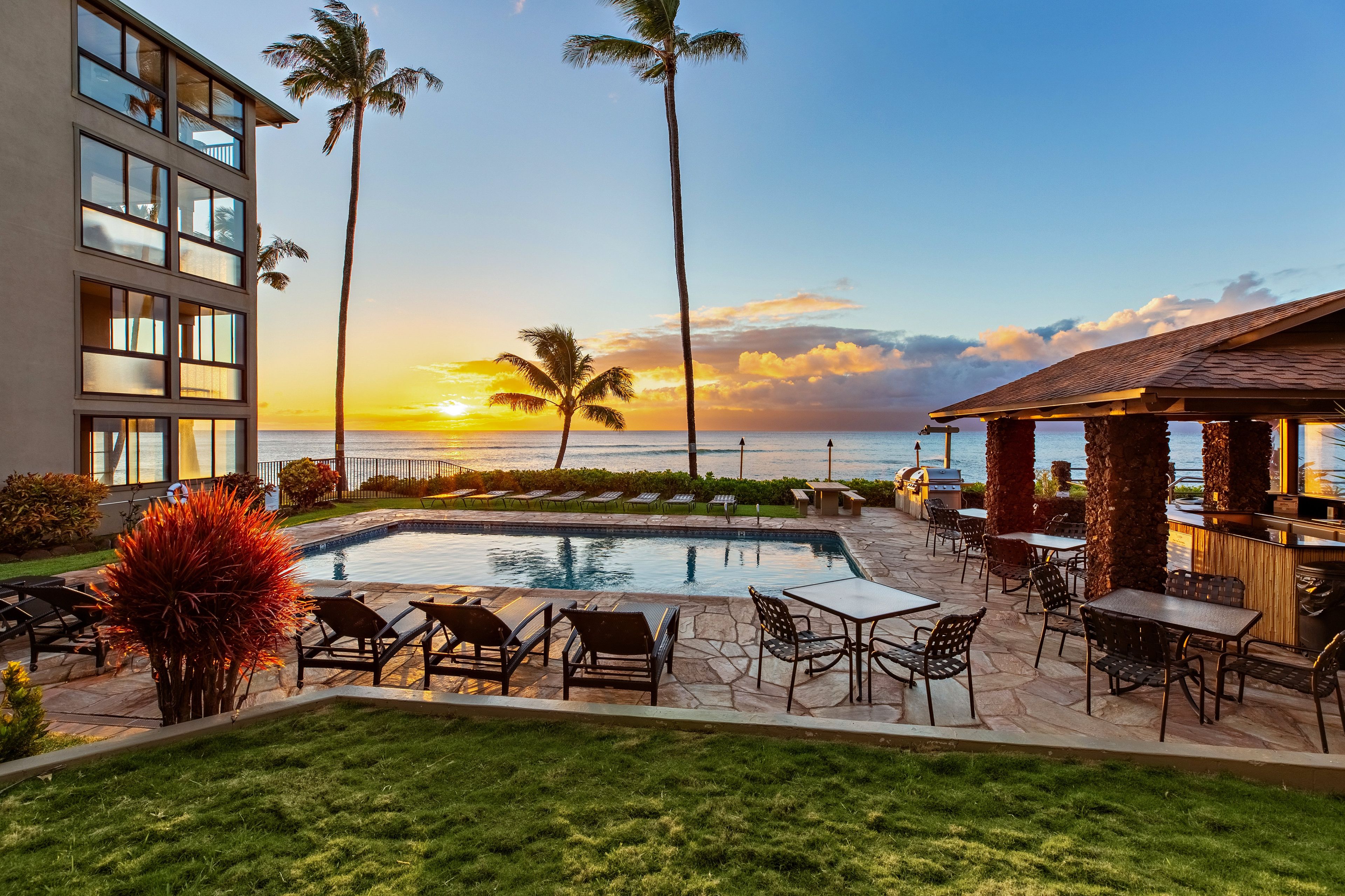 A pool area with lounge chairs and a view of the ocean at sunset.