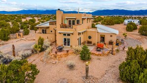 A modern two-story house with a patio area, surrounded by a desert landscape and mountains in the background. - Amazing Views, Hot Tub, Pool, Sauna, Gourmet Kitchen, Master Suites!  (Santa Fe)