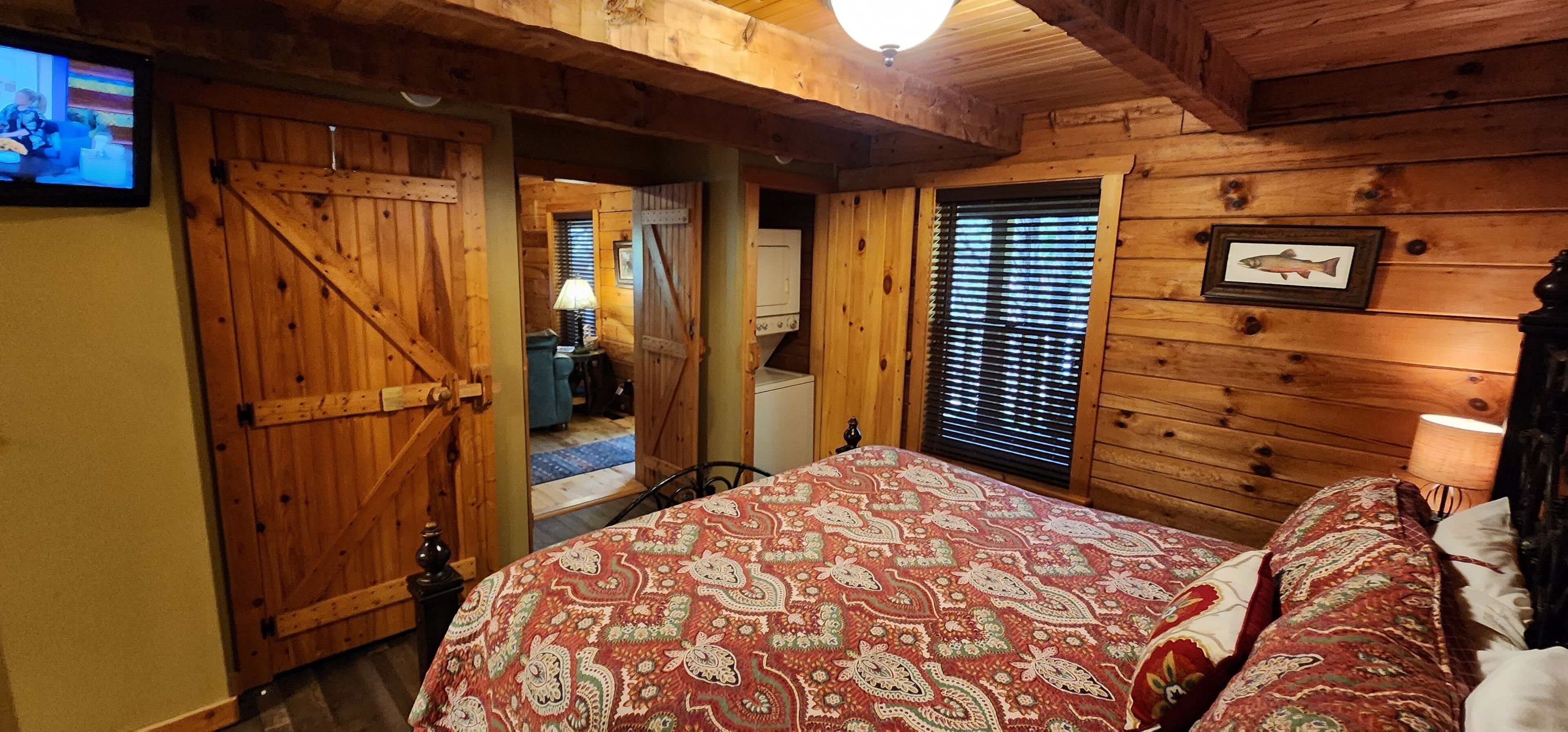 Un dormitorio de cabaña de madera con una cama, un televisor y una ventana con persianas.