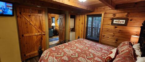 Une chambre dans une cabane en bois, avec un lit, une télévision et une fenêtre équipée de stores.