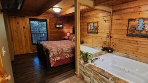A log cabin bedroom with a bed, a stone wall, a bathtub, and wooden walls. - Lovesong #9- Charming & Clean Log Cabin!! (Sevierville)