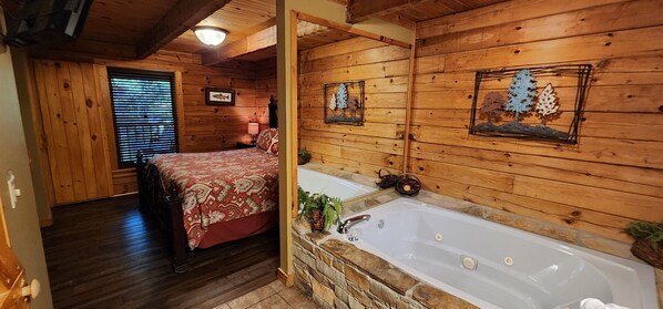 A log cabin bedroom with a bed, a stone wall, a bathtub, and wooden walls.
