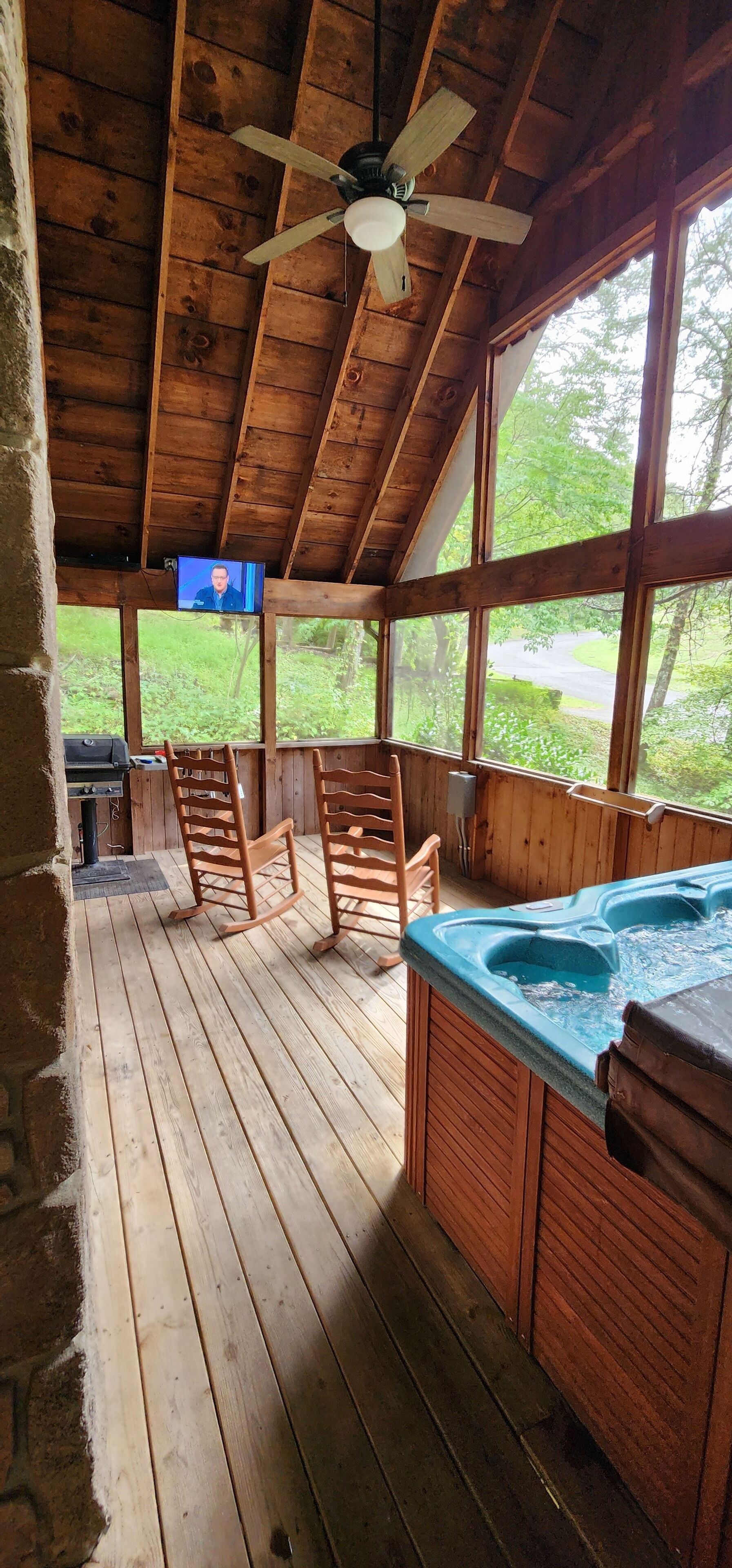 A wooden deck with rocking chairs, a hot tub, and a television screen.