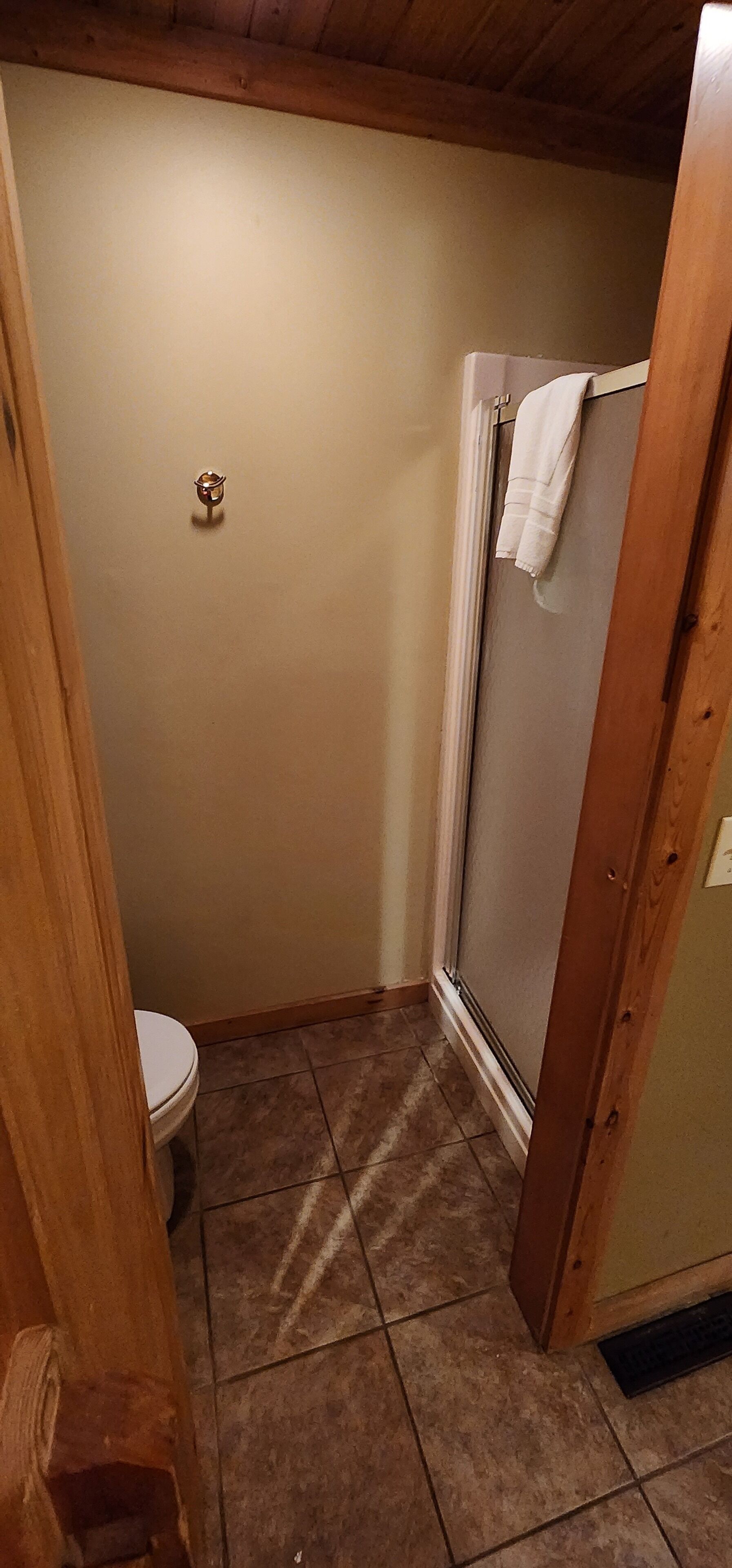 Un bagno piccolo con il water, una doccia con un asciugamano appeso e un soffitto in legno.
