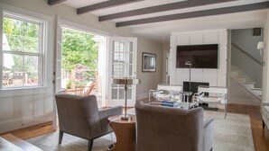 A spacious living room with a fireplace, large windows, and a staircase leading to an upper floor. - Luxurious 5 bedroom home with hot tub and pool in prime location (Nantucket)