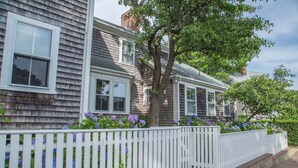 A row of two-story houses with white picket fences, brick steps, and purple hydrangea flowers. - Luxurious 5 bedroom home with hot tub and pool in prime location (Nantucket)
