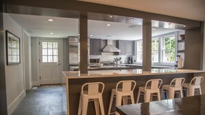 A modern kitchen with grey cabinets, a central island with bar stools, and a large window providing natural light. - Luxurious 5 bedroom home with hot tub and pool in prime location (Nantucket)