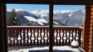 Un balcón con baranda de madera y suelo cubierto de nieve, con vistas a un paisaje montañoso y picos nevados.