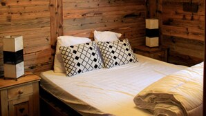 Una habitación tipo cabaña de madera con una cama, dos lámparas de noche y un colgador de techo.