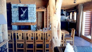Un interior rústico de madera con chimenea de piedra, mesa y sillas de madera.
