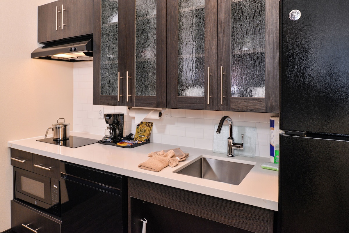 A modern kitchen with dark wooden cabinets, a stainless steel sink, and a black refrigerator.