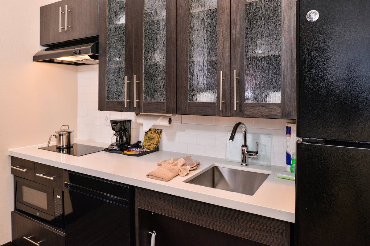 A modern kitchen with dark wooden cabinets, a stainless steel sink, and a black refrigerator.