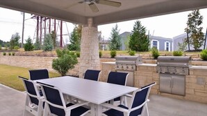 An outdoor patio with a white table and blue chairs, a ceiling fan, and a grill.