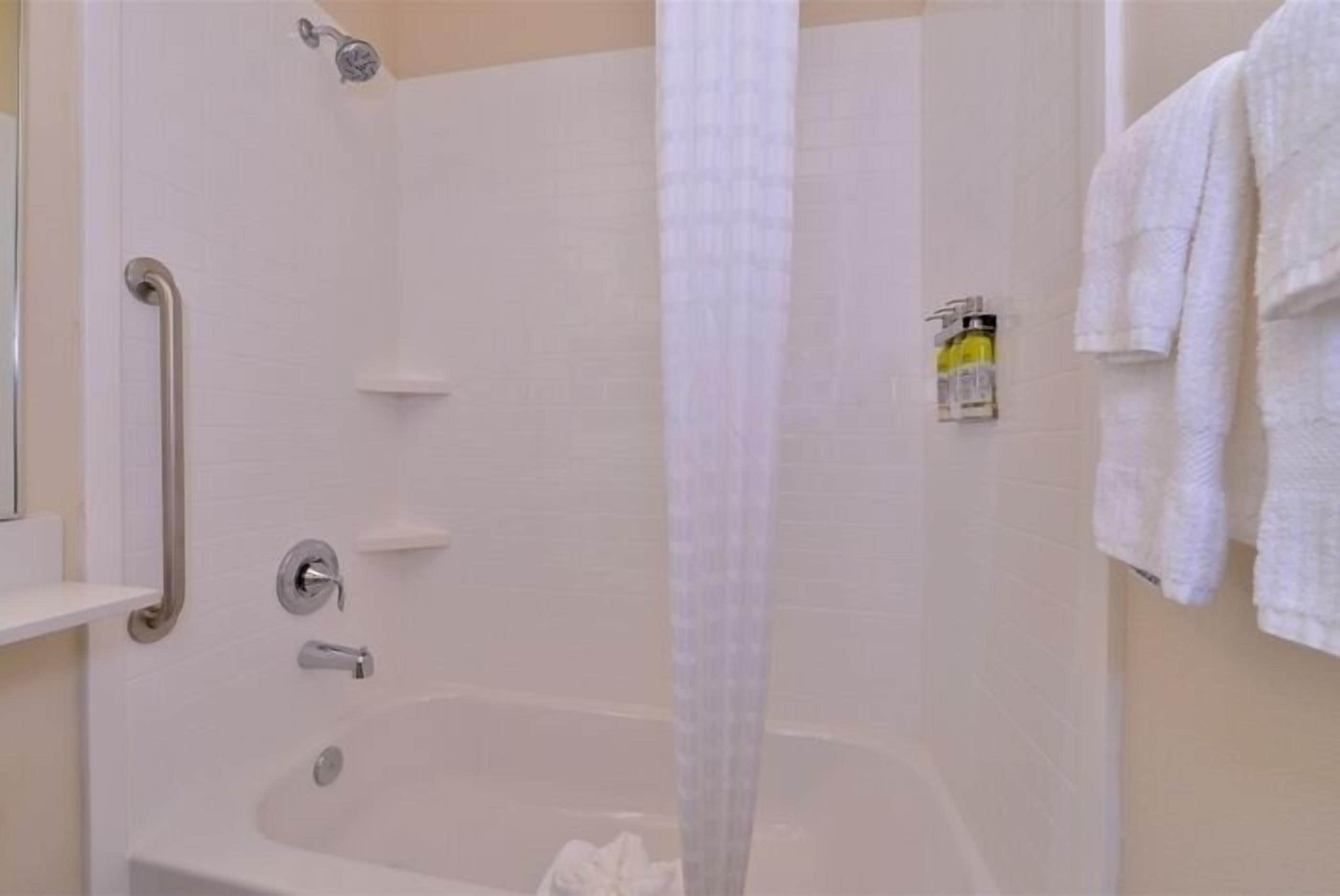 A bathroom with a walk-in shower, grab bars, a bathtub, and a towel rack.