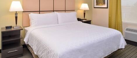 A hotel room with a large bed, two bedside tables with lamps, a small drawer unit, and a framed picture on the wall.