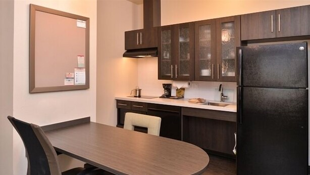 Une cuisine moderne avec des meubles de rangement en bois foncé, un réfrigérateur noir et un plan de travail blanc.
