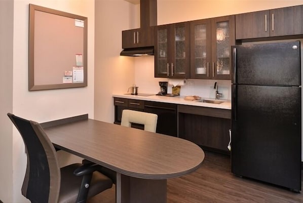 A modern kitchen with dark wooden cabinets, a black refrigerator, and a white countertop.