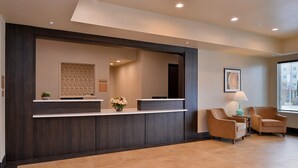 A reception area with a dark wood reception desk, a potted plant, and two armchairs.