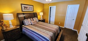 Una camera da letto con un letto, due comodini, una lampada, un quadro incorniciato e una porta.