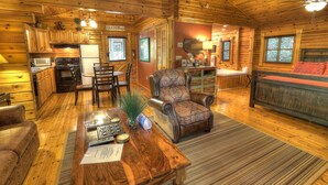 L’intérieur chaleureux d’un chalet en bois comprend une table à manger en bois, un fauteuil en cuir et un coin cuisine équipé d’un réfrigérateur et d’un four à micro-ondes.