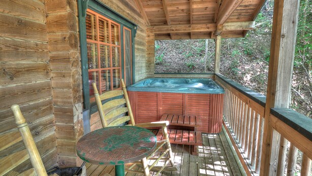 Une cabane en bois avec un bain à remous, une terrasse en bois et une table avec des chaises.