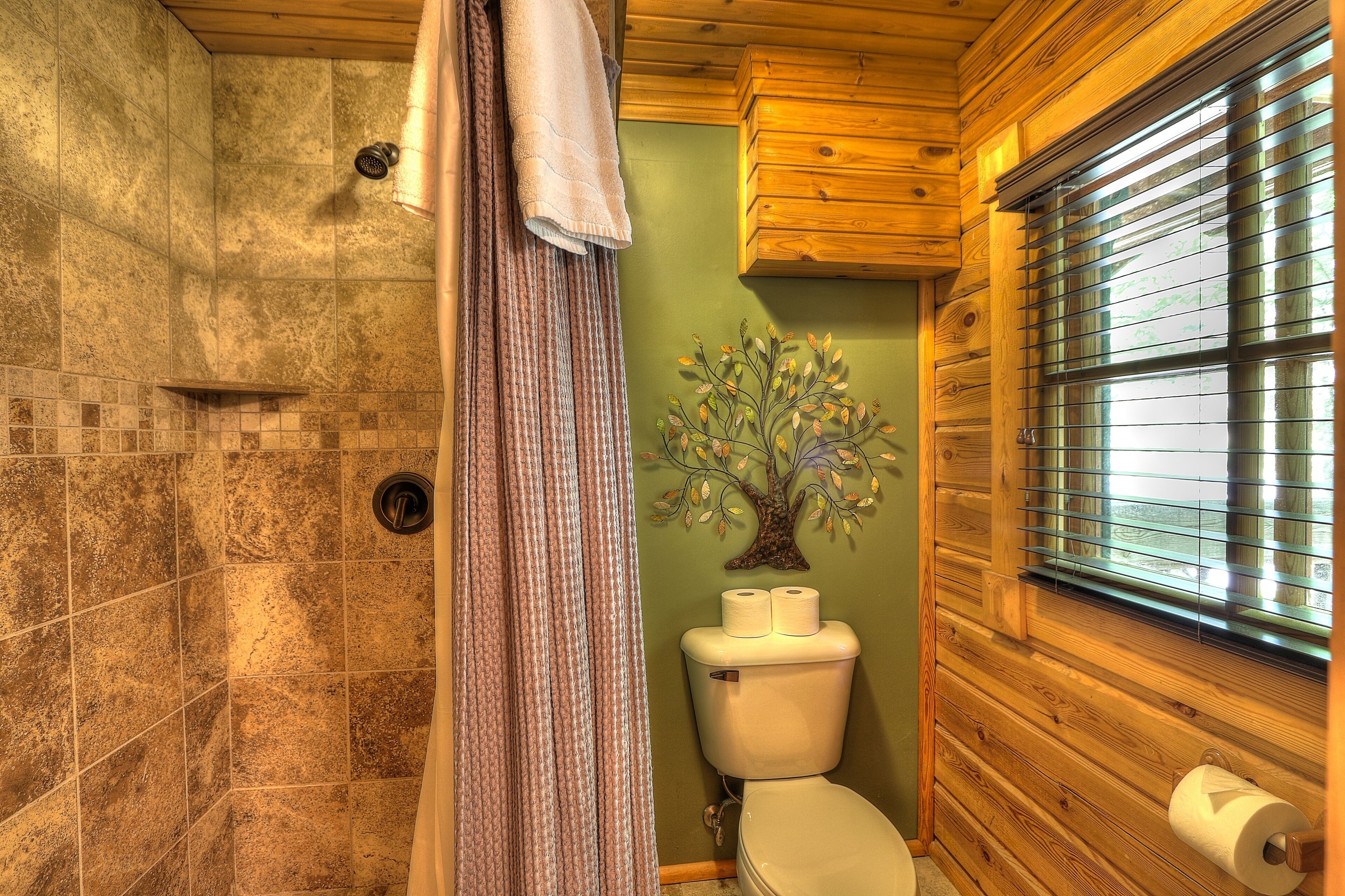 Ein Badezimmer mit Dusche, Toilette und Fenster mit Jalousien.