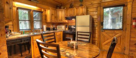 Cocina de cabaña de madera con una mesa de comedor, sillas, un refrigerador y una estufa.