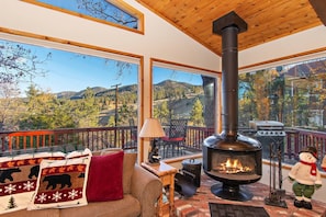Una habitación acogedora con chimenea, ventanas amplias y vistas a un paisaje montañoso.