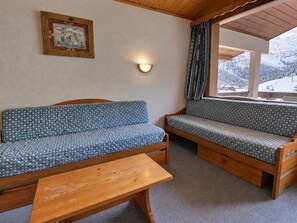 A cozy room with a wooden bench, two patterned sofas, a wall-mounted light, and a window with a view of snow-covered mountains. - Comfortable with large south terrace, pets allowed (Méribel)