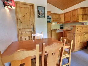 Une table de salle à manger en bois avec des chaises, un coin cuisine avec des placards en bois et une porte dotée d’une poignée.