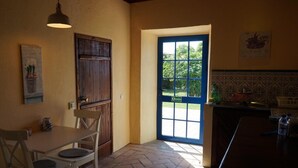 A kitchen with a wooden table, chairs, a hanging light fixture, a blue door, and a tiled backsplash.