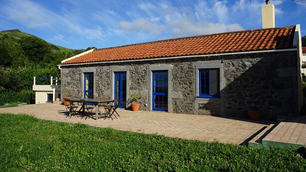 A stone building with a tiled roof, blue doors, and a patio area with a table and chairs.