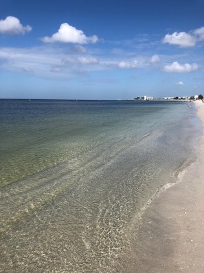 A beach with clear shallow waters and a sandy shore.