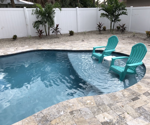 A swimming pool with two turquoise chairs and a small table.