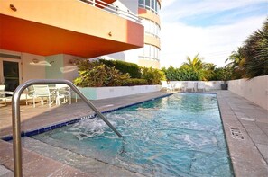 Relax by the rectangular pool with a metal ladder, surrounded by lush greenery and potted plants.