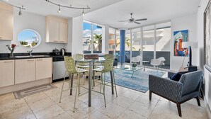 Una cocina moderna con comedor, ventanas amplias y vistas a palmeras.