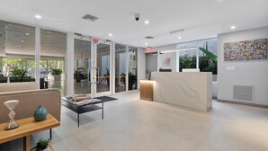 Un lobby moderno con puertas de vidrio, una recepción y un área de estar con una mesa de centro y elementos decorativos.