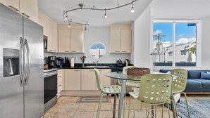 Una cocina moderna con un refrigerador de acero inoxidable, armarios de madera y un comedor con mesa de vidrio y sillas verdes.