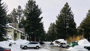 A snowy parking lot with several cars and a building in the background.