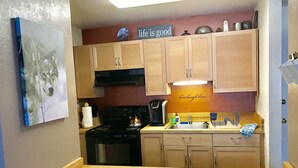 A compact kitchen with wooden cabinets, a stove, and a coffee maker. A sign on the wall reads "life is good."