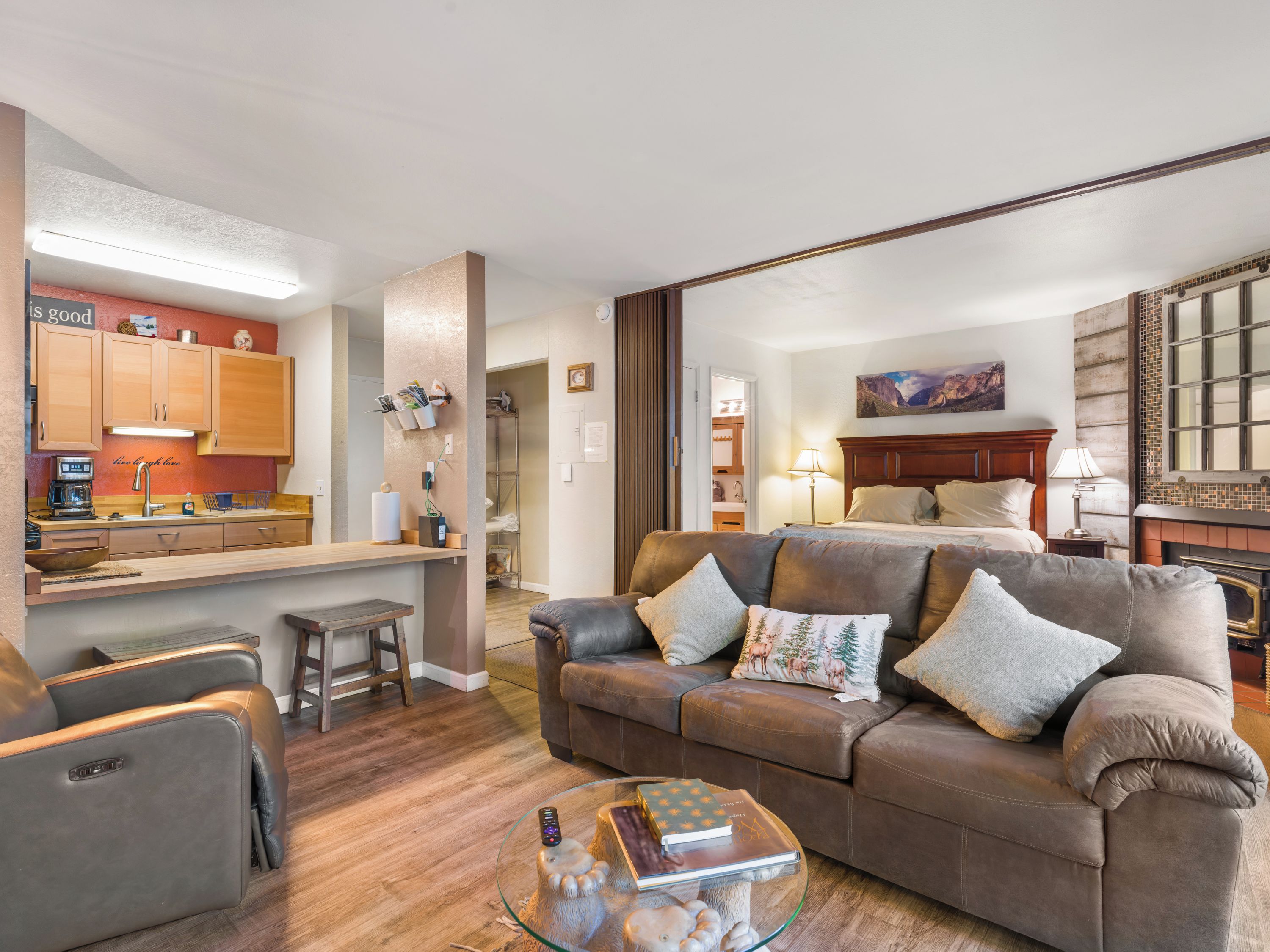 Ein modernes Wohnzimmer mit einer Ledersofa, einem Glastisch und einer Küchenzeile mit Holzschränken und einer Arbeitsplatte.