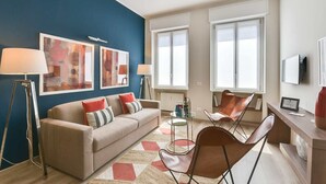 En moderne stue med en blå accentvæg, en beige sofa, to lænestole, et sofabord og kunstværker.