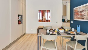 En moderne spiseplads med et bord dækket til fire personer, et vindue med udsigt og et billede på væggen.