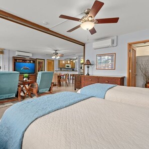 A hotel room with a bed, a ceiling fan, a TV, a desk, and a kitchenette.