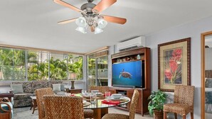 A spacious living room with a ceiling fan, a television, and a dining area with wicker chairs.
