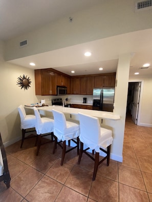 A modern kitchen with a central island, wooden cabinets, and a stainless steel refrigerator.