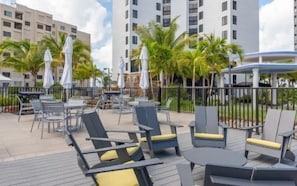 An outdoor patio with lounge chairs and umbrellas, surrounded by palm trees and high-rise buildings.