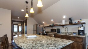 A kitchen with a granite island, stainless steel appliances, and wooden cabinetry. - Glacier Hideaway with Mountain Views close to Glacier Park (West Glacier)
