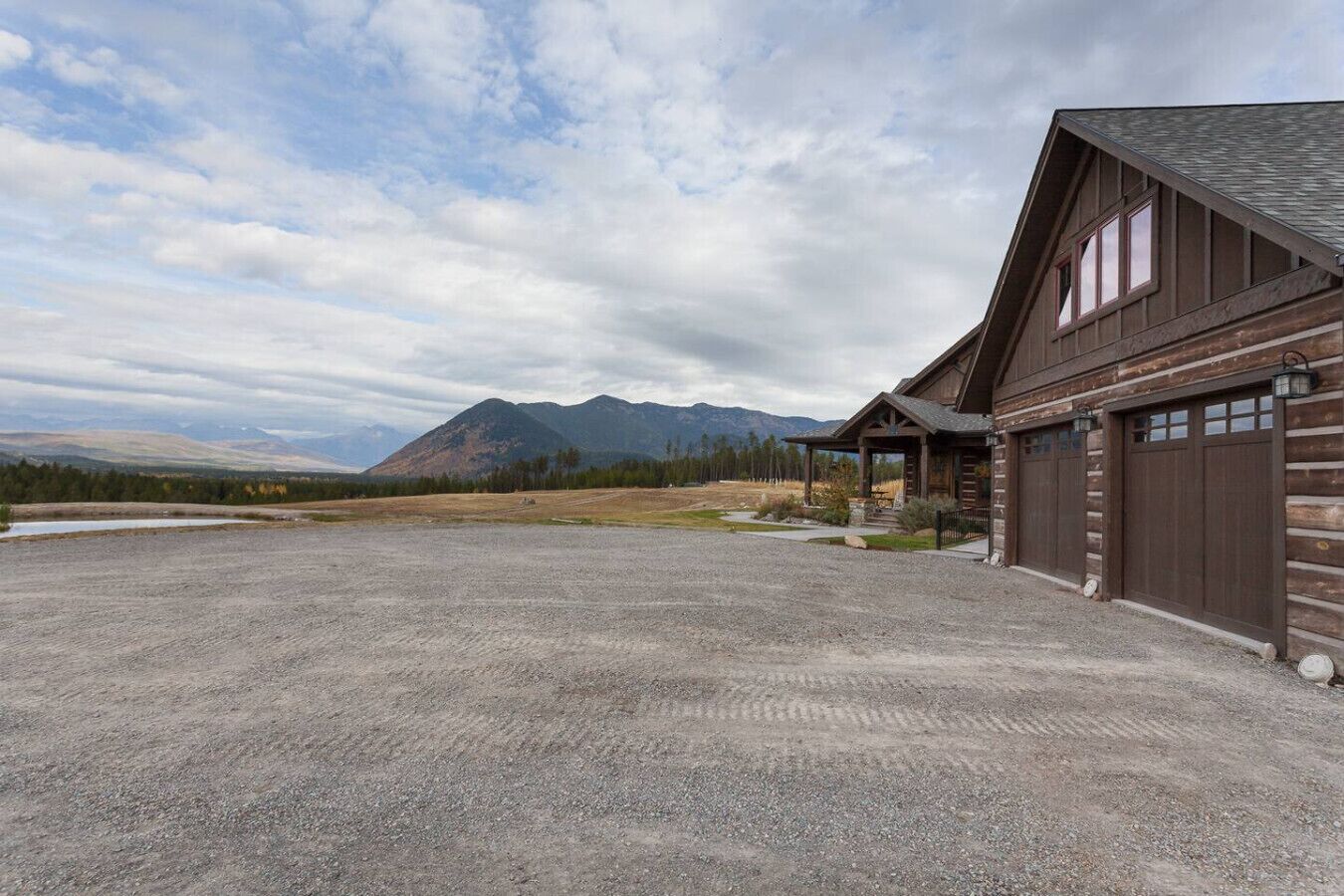 A log cabin with a gravel driveway and a mountain backdrop.